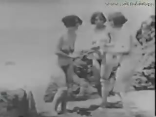 1928 vintāža ar a puisis spiegošana meitenes par the pludmale